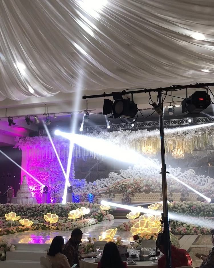 Wedding reception venue with bright white spotlights, purple lighting, and white floral decor.