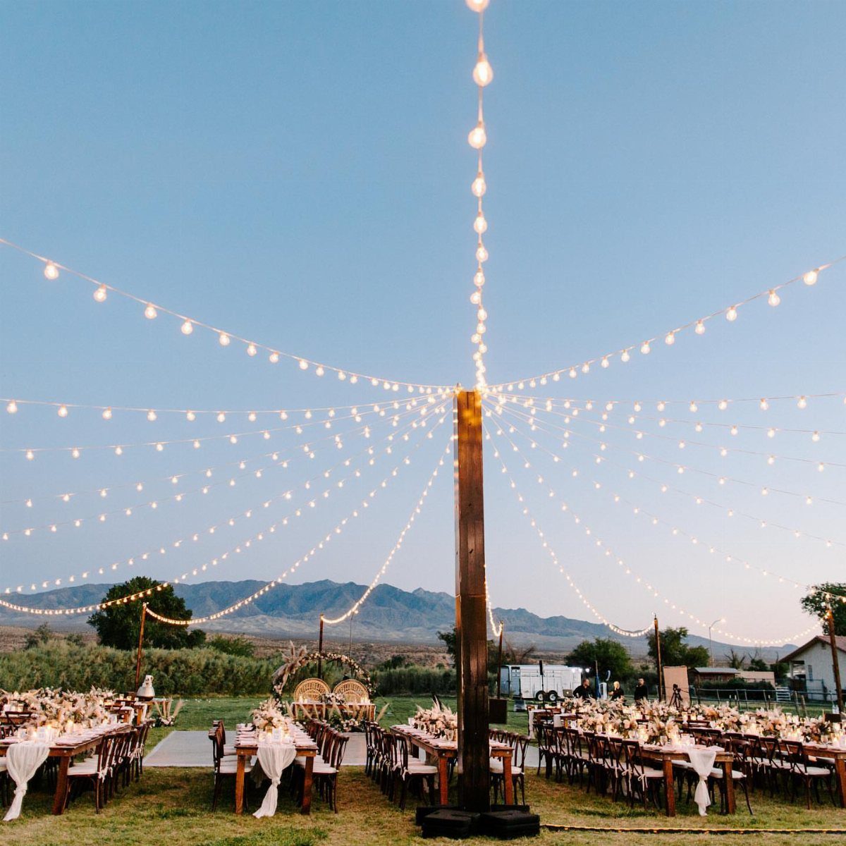 String lights radiating from a central pole over outdoor wedding reception tables.