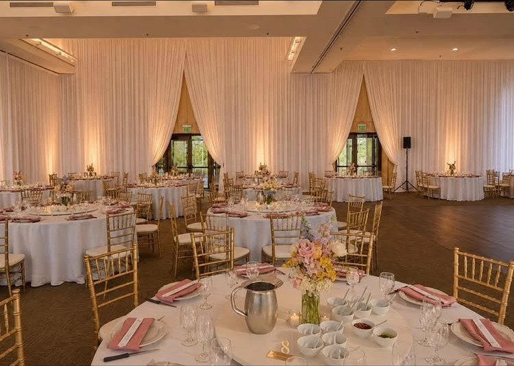 Wedding reception hall with white draped walls illuminated by warm amber uplighting.