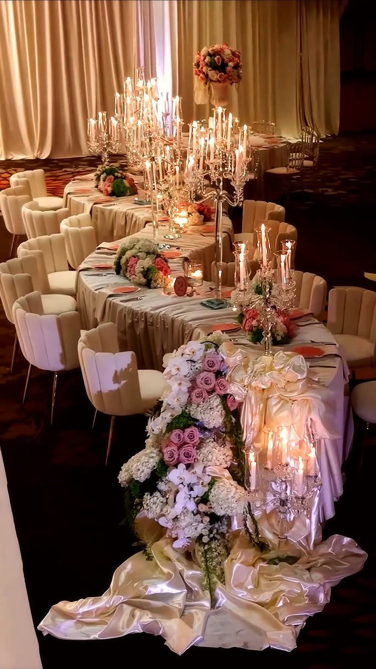 Long wedding head table with white linens, crystal candelabras, and pink floral arrangements.