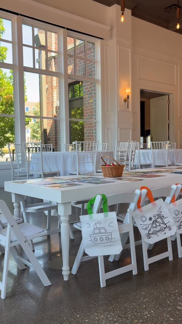 White rectangular table with children's activity bags hanging from white folding chairs.