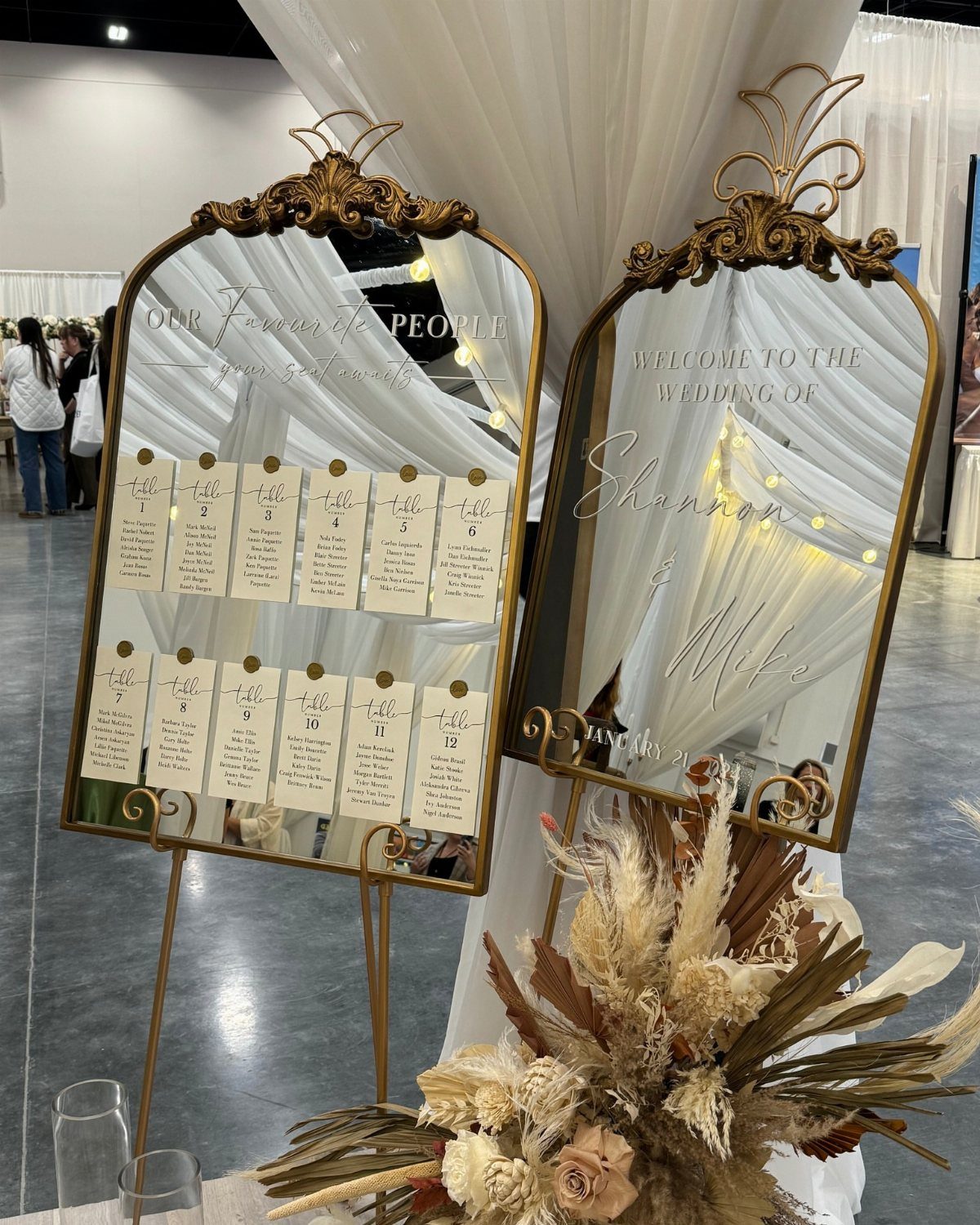 Gold framed mirrors displaying a wedding seating chart and welcome sign with dried flowers.