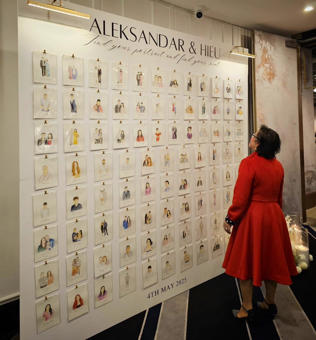 Woman in red dress looking at a wall of guest portrait seating assignments.