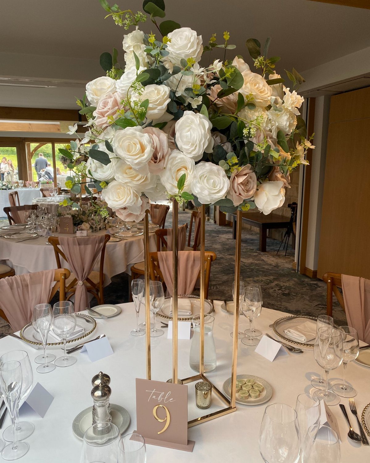 Large white and cream rose centerpiece on a gold stand at wedding table