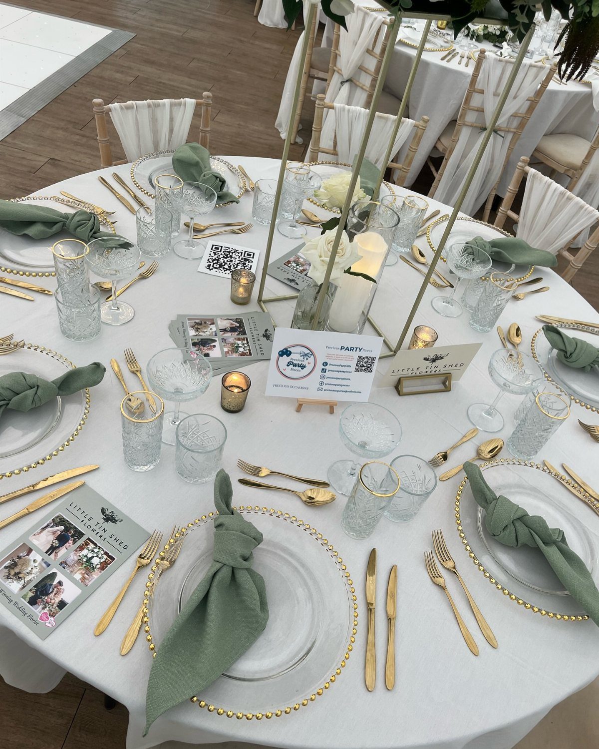 Round wedding table with gold-rimmed plates, gold cutlery, and sage green napkins.