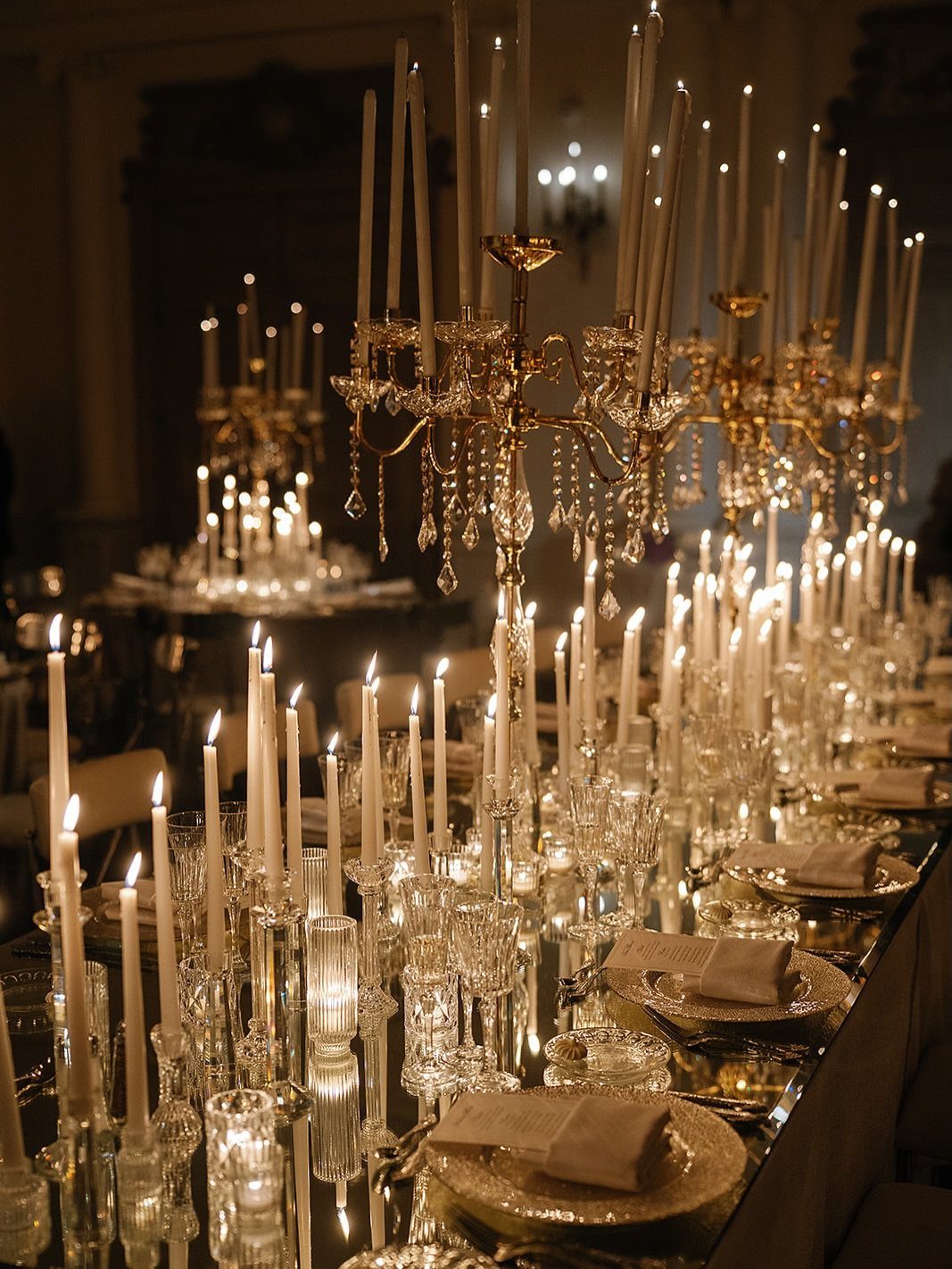 Long dinner table decorated with gold candelabras, white candles, and elegant place settings.