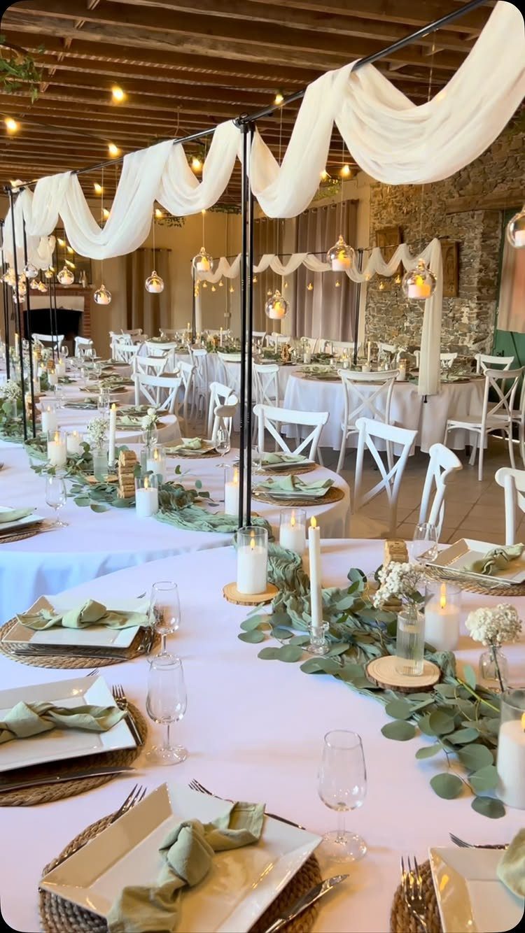 Wedding reception tables with white linens, eucalyptus greenery, and glowing hanging lanterns.