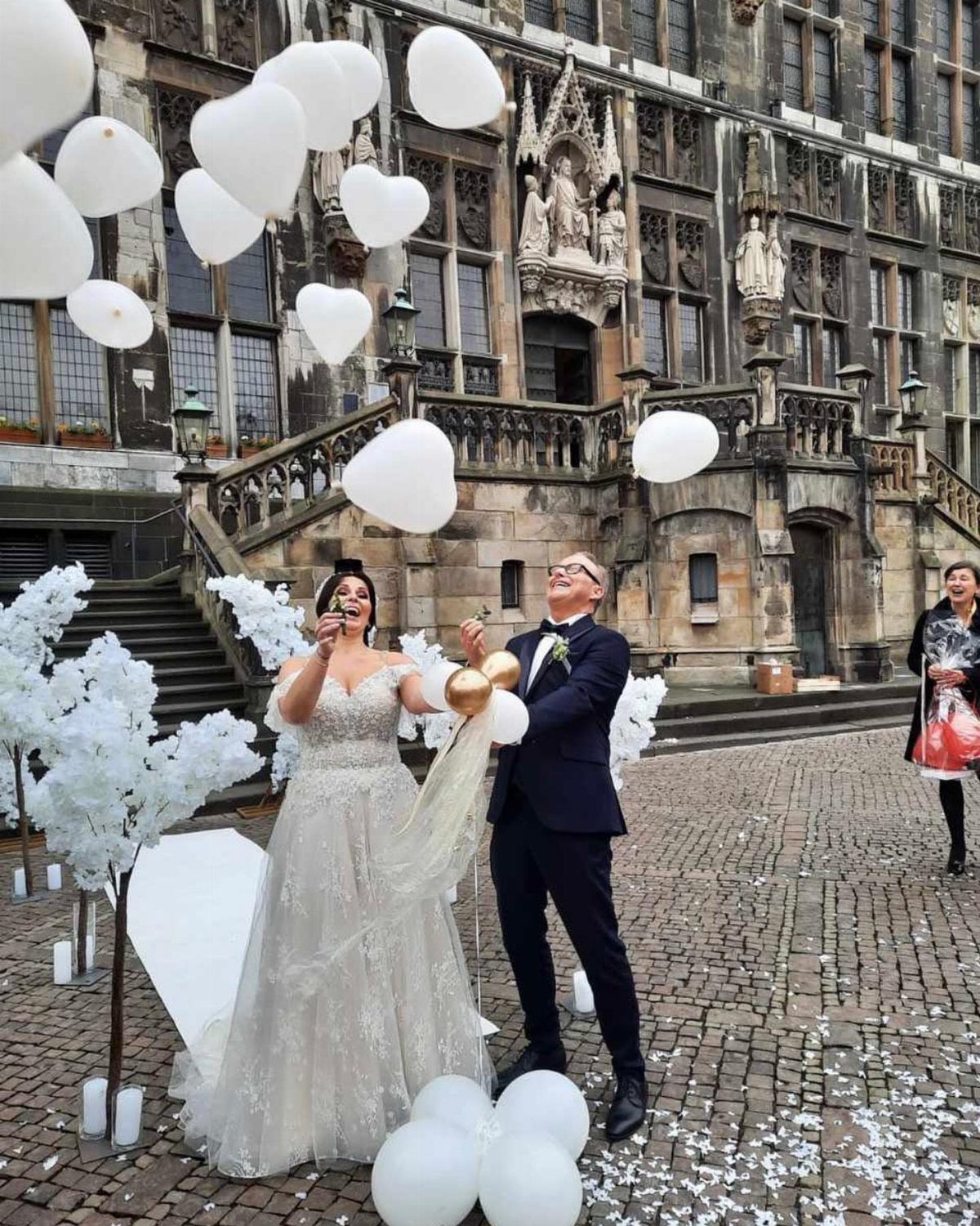 Bride and groom releasing white heart-shaped balloons in a gothic stone courtyard.