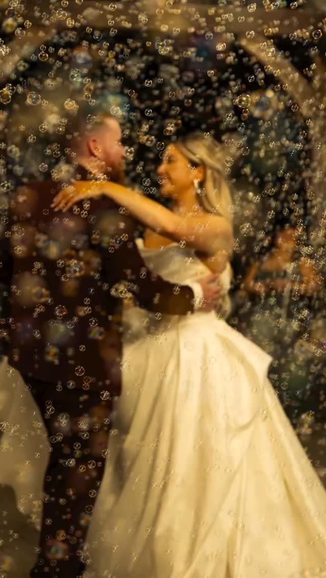 Bride and groom embracing while surrounded by floating bubbles during their wedding exit.
