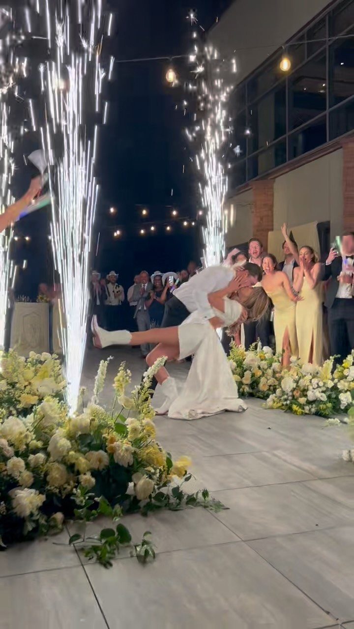 Bride and groom kissing between tall cold sparkler fountains and white flowers.