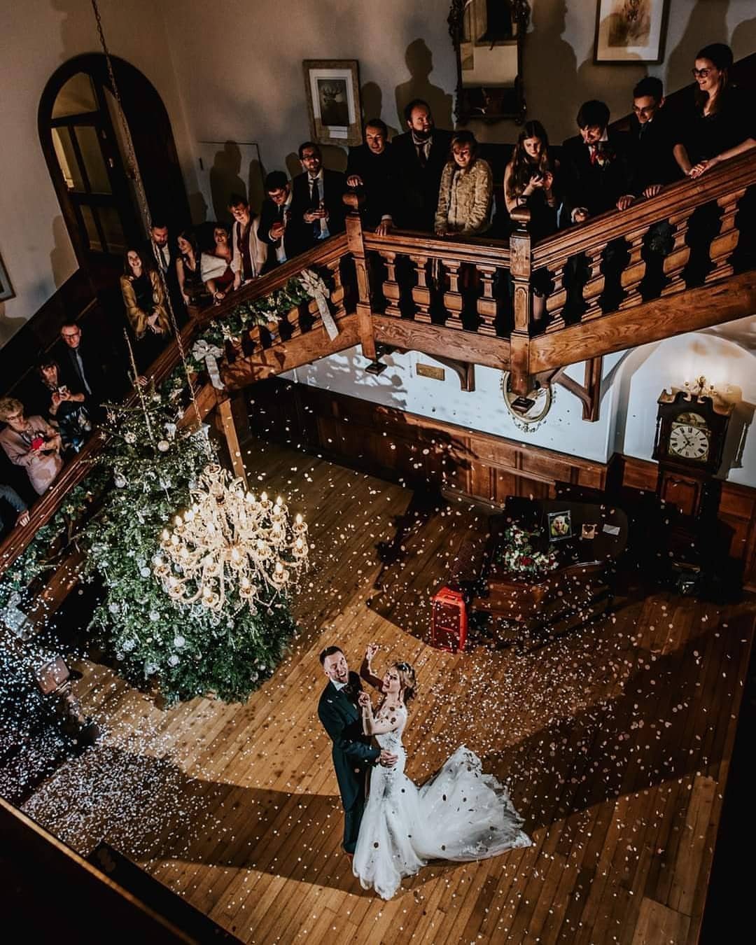 Bride and groom embracing under a shower of white confetti in a hall.