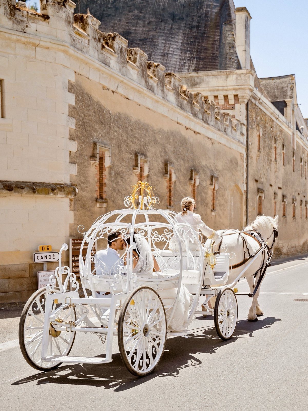 Bride and groom kissing in an ornate white horse-drawn carriage on a street