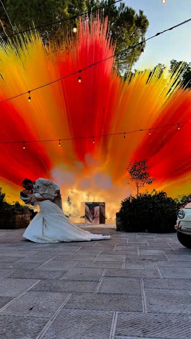 Bride and groom kissing in front of dramatic red and yellow smoke plumes.