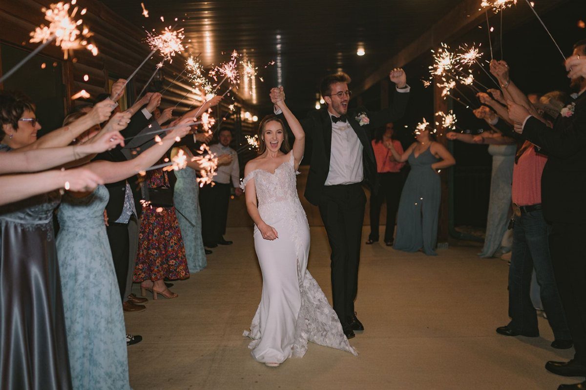 Bride and groom walking through a tunnel of guests holding glowing sparklers