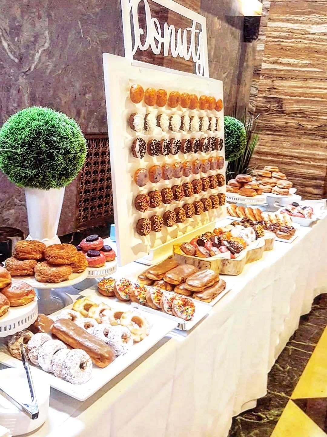 Donut bar with a vertical display wall and platters of assorted donuts.