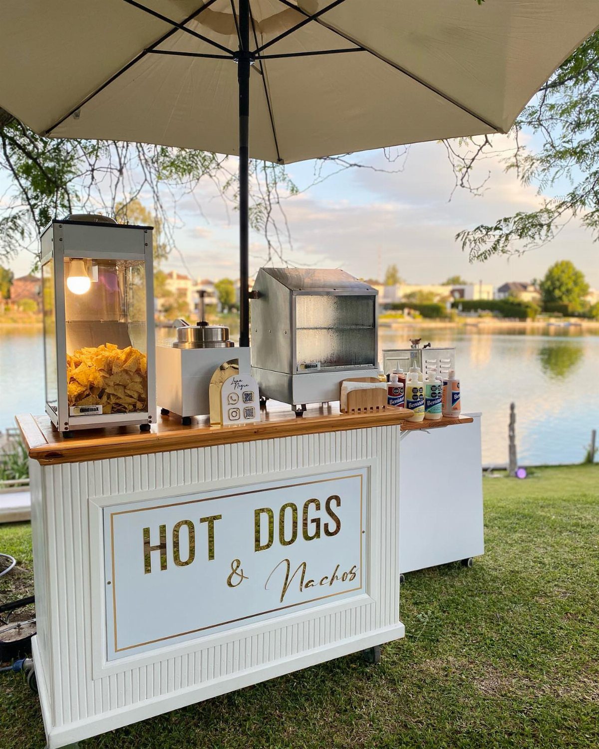 Hot dog and nacho station with a popcorn machine under a white umbrella.