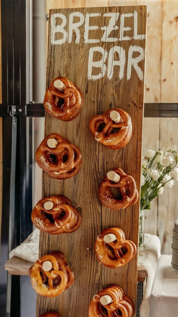 Soft pretzels hanging on a wooden board labeled Brezel Bar with dipping sauce.