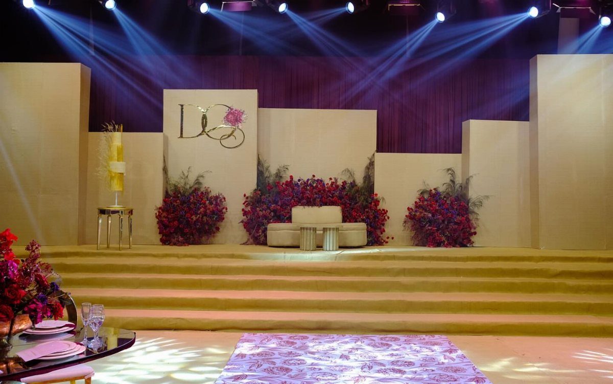 Wedding stage with cream geometric panels, red flowers, and blue spotlights overhead.