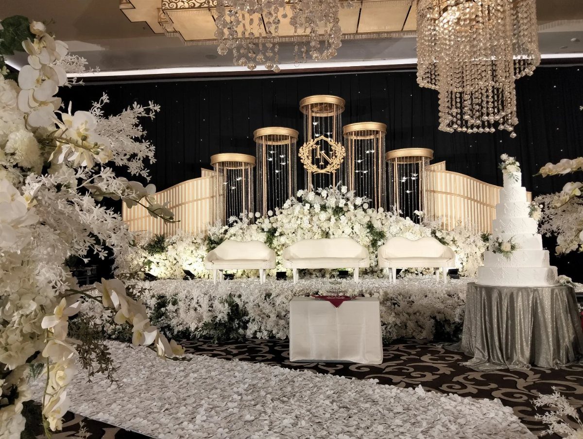 Wedding stage with glowing golden pillars, white flowers, and white sofas.