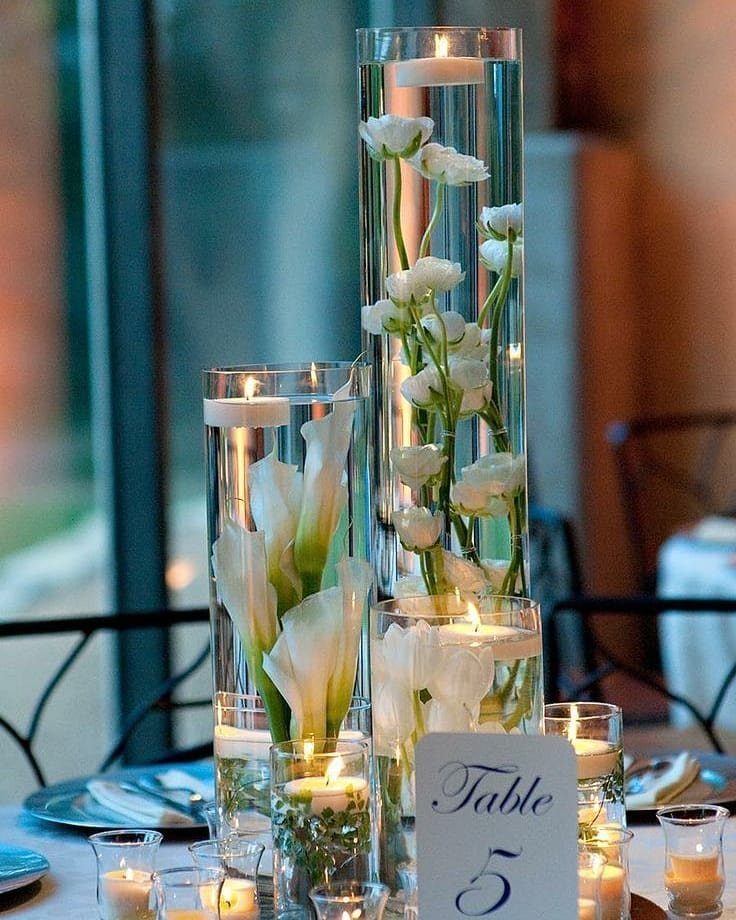 Tall glass cylinder vases with white calla lilies and floating white candles.