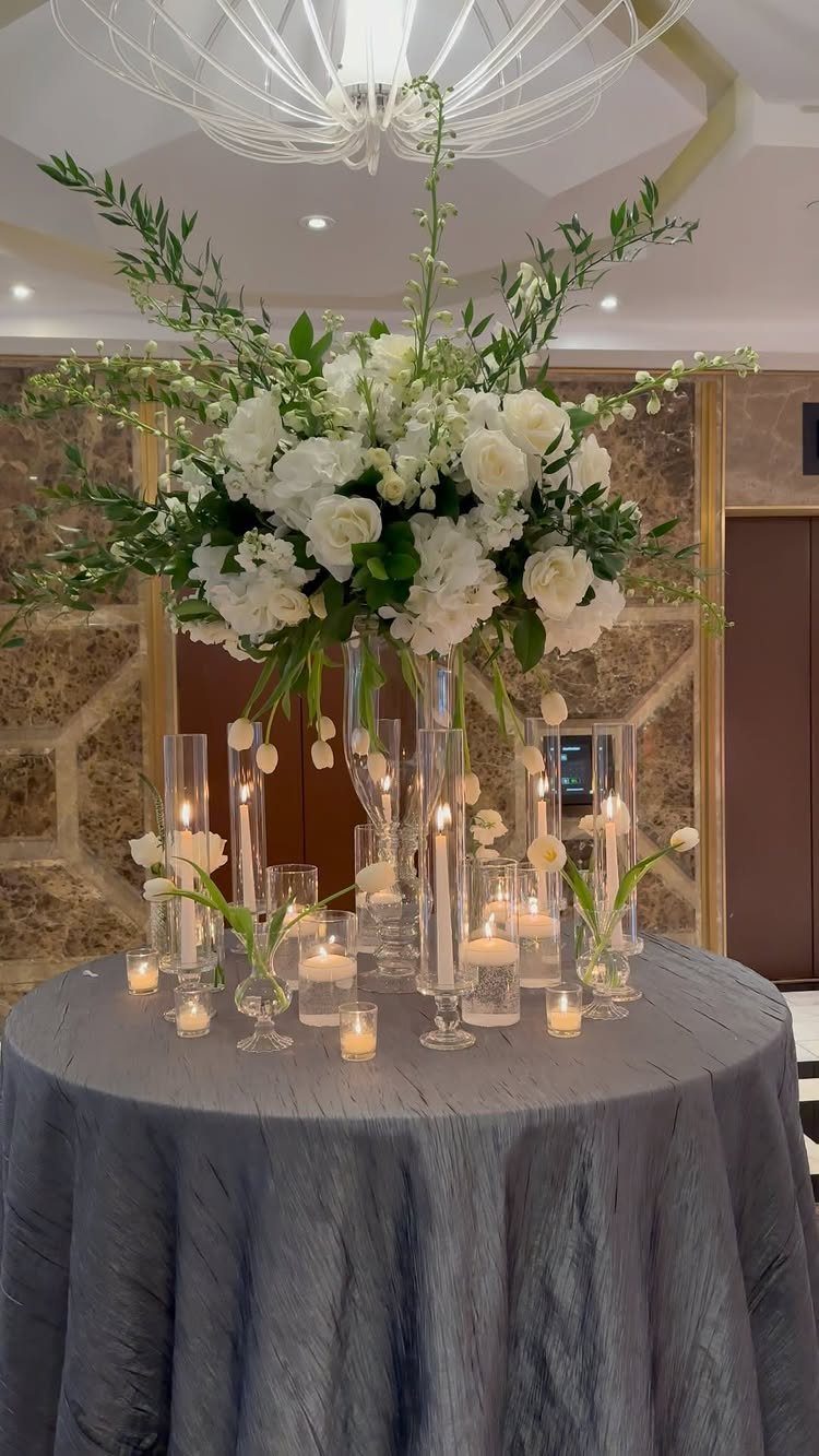 White rose and hydrangea centerpiece surrounded by floating candles on a grey table.