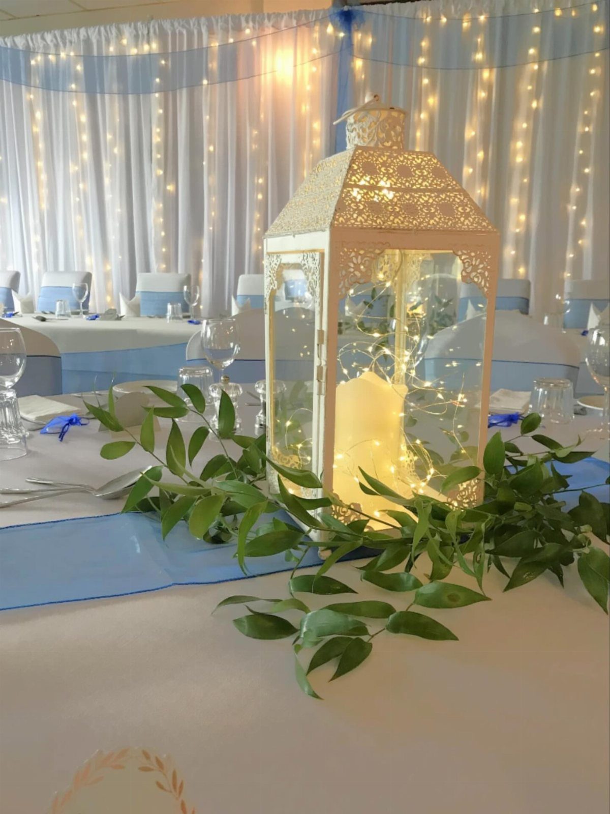 White decorative lantern with fairy lights and greenery on a wedding table