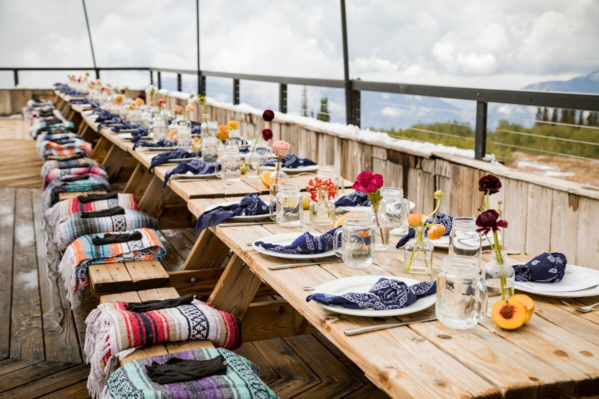 Wooden outdoor table set with wildflowers in glass jars and blue napkins.