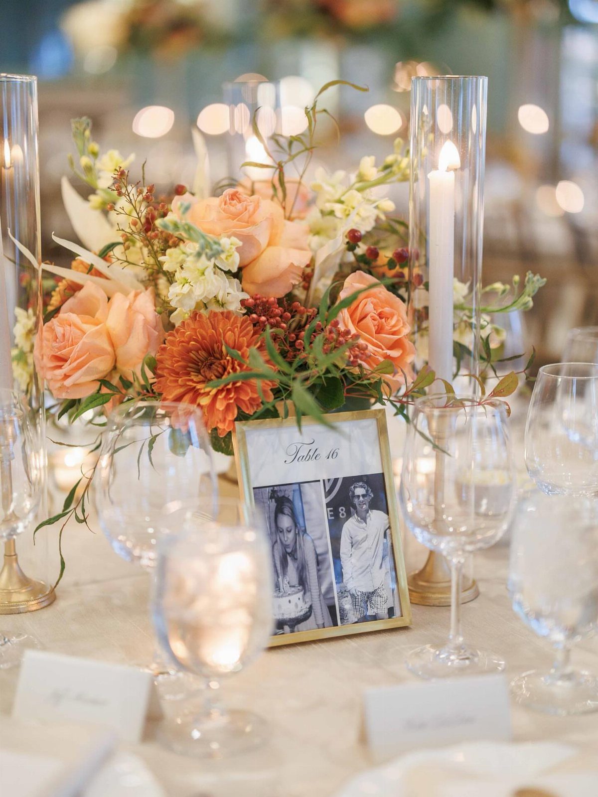 Orange and white floral arrangement with tall candles on a wedding table.