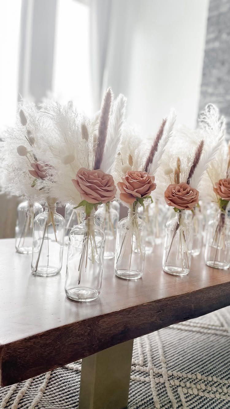 Dusty rose roses and white pampas grass in small glass vases on a table.