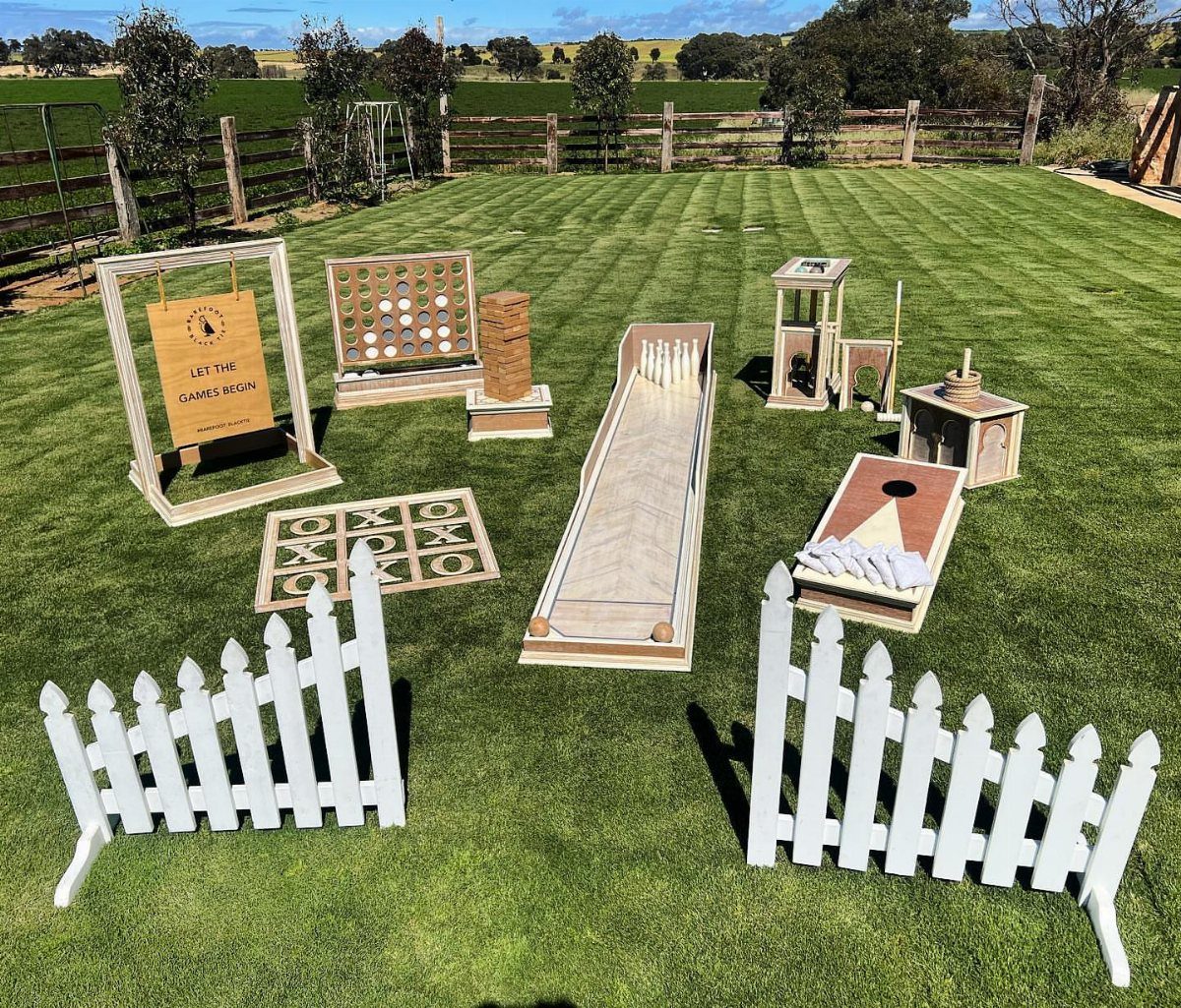 Wooden outdoor lawn games arranged on green grass with a white picket fence.