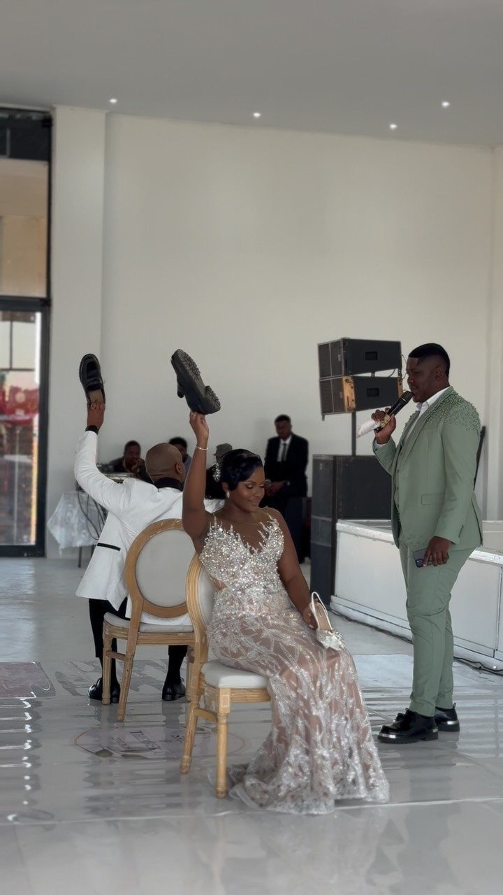 Bride and groom sitting back-to-back holding up shoes during a wedding shoe game.