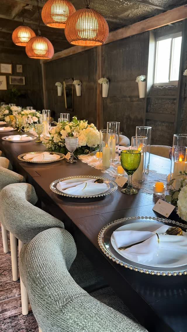Wedding table setting with white plates, silver chargers, white flowers, and green glassware.