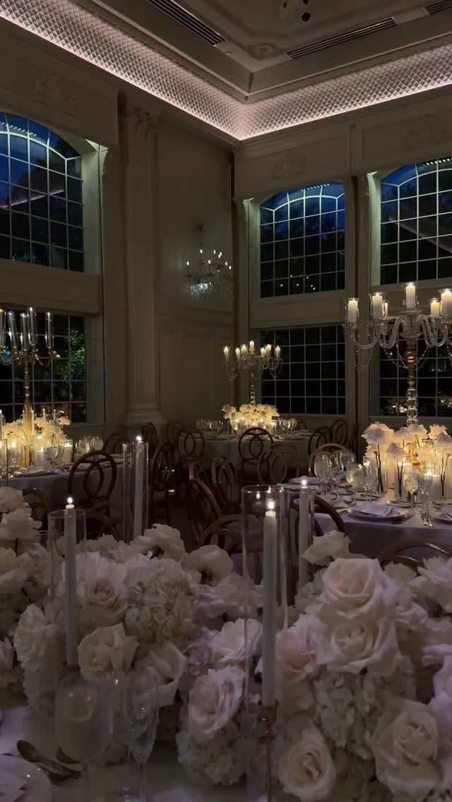 Gold candelabras and white rose centerpieces on elegant wedding tables in a ballroom.