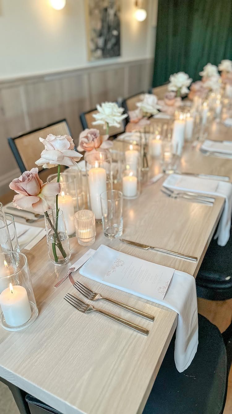 Wedding table setting with pale pink roses in vases and white glowing candles.