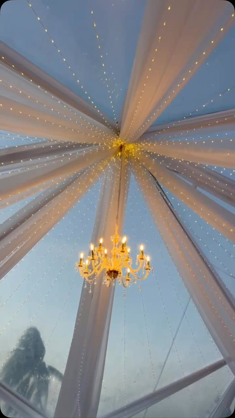White draped tent ceiling with fairy lights and a gold chandelier