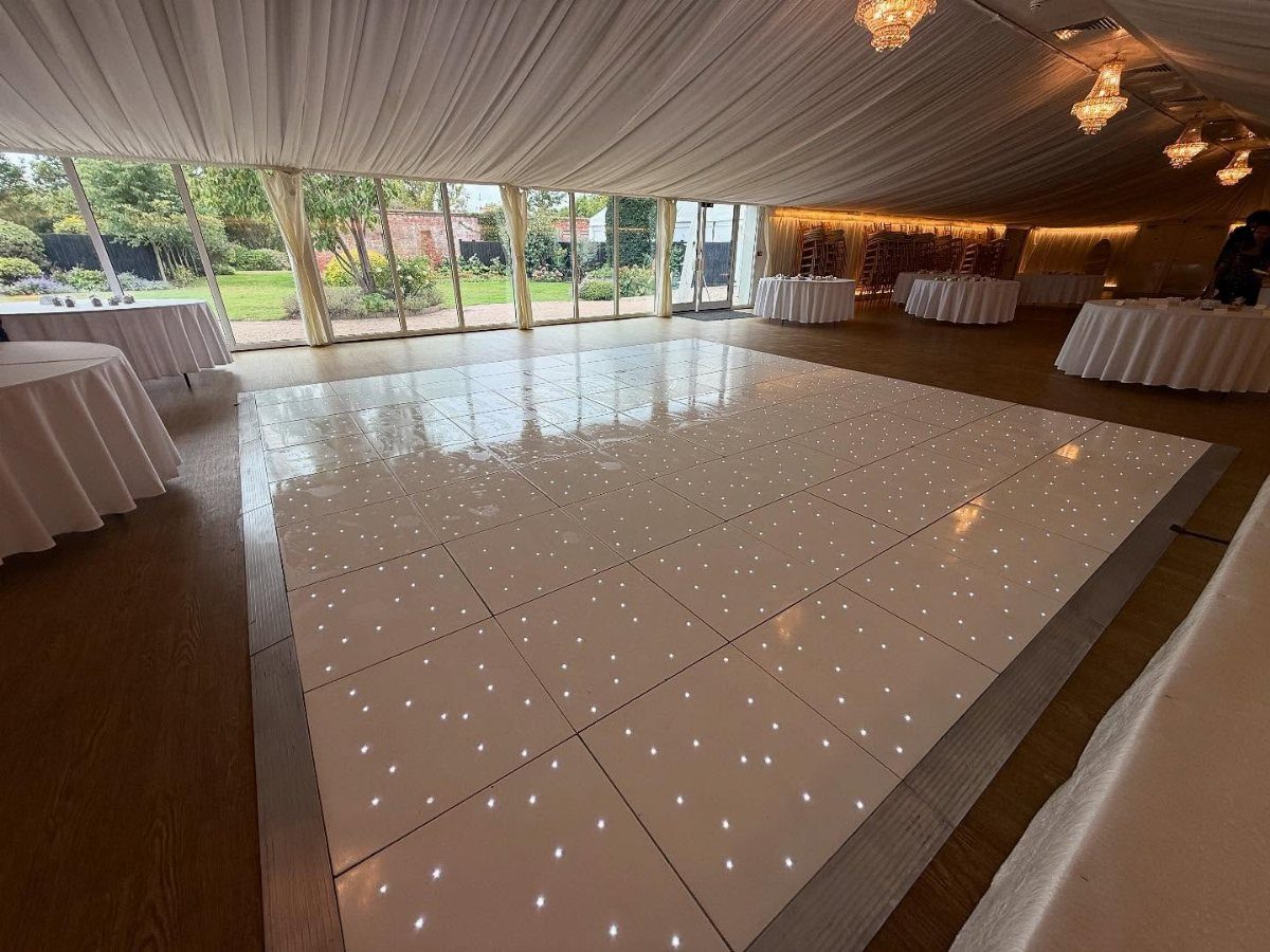 White starlit dance floor inside a draped wedding tent with white tables