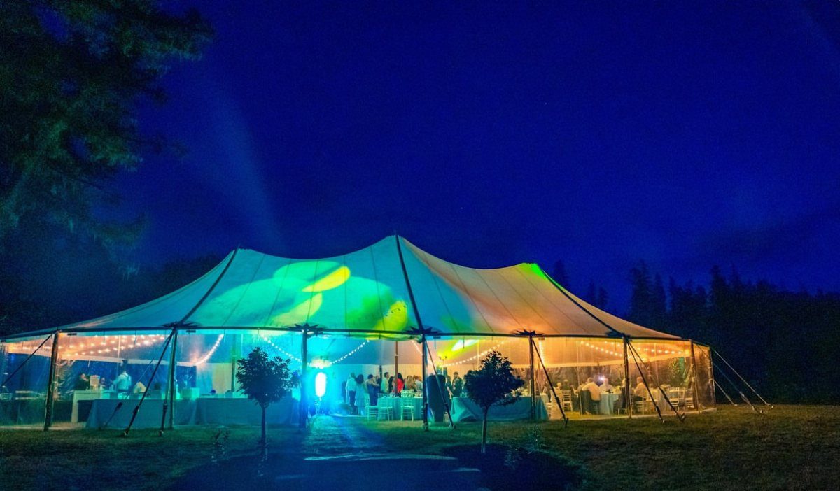 Large white event tent illuminated with colorful lights at night on a field