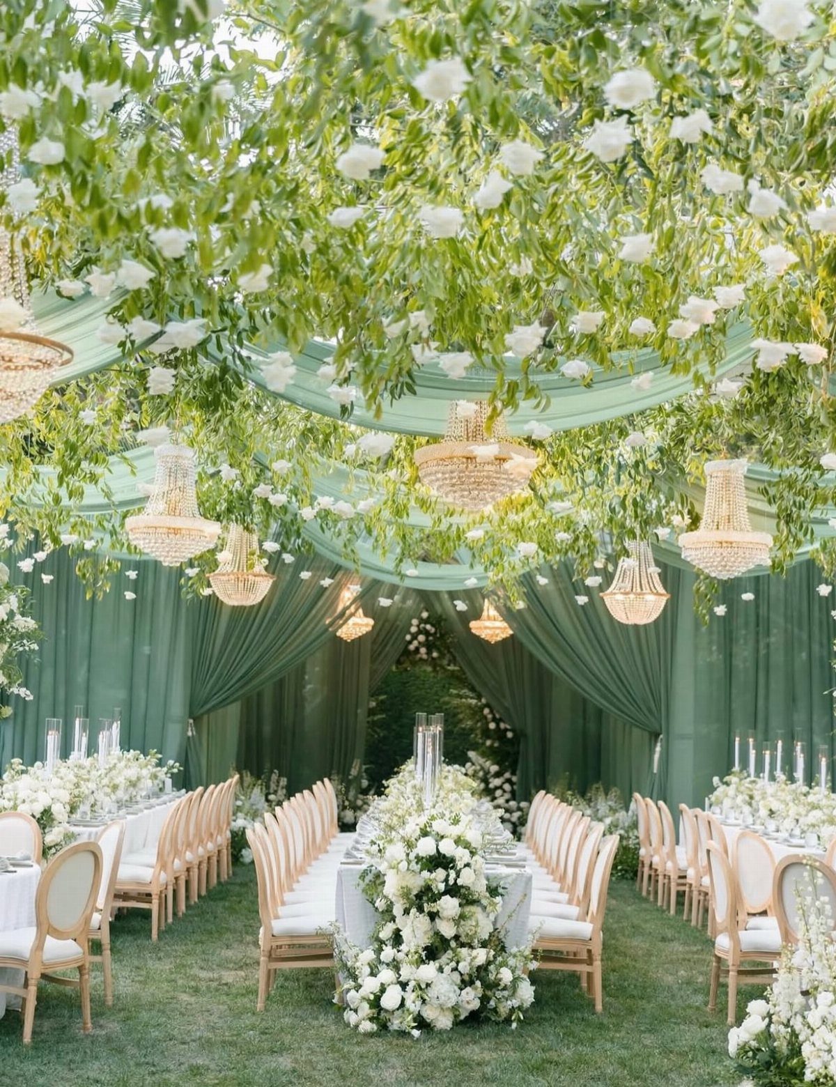 Hanging greenery and white flowers suspended from a green draped wedding tent ceiling.