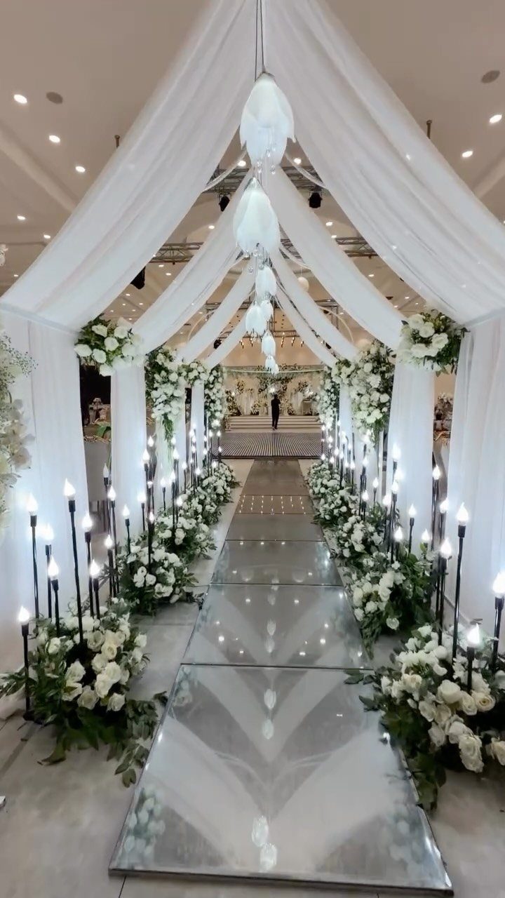 Mirrored wedding aisle with white floral arrangements and black candle holders under white draping.