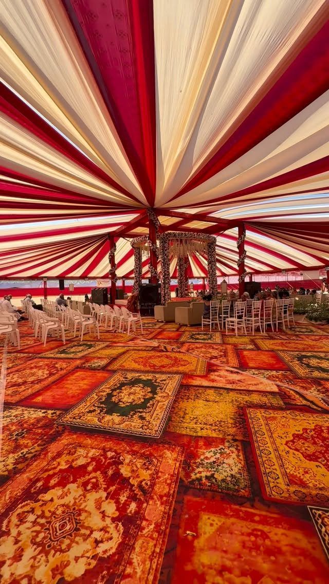 Red and cream draped tent ceiling over colorful rugs and white wedding chairs.