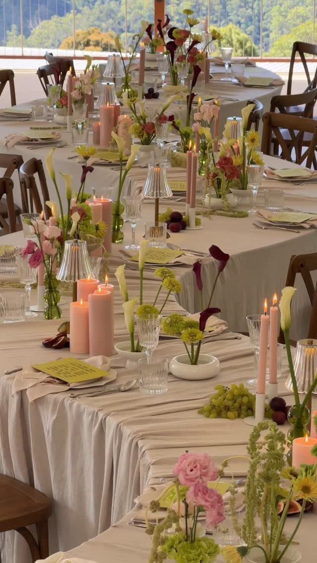 Long tables with beige linens featuring varied floral centerpieces and pink taper candles.