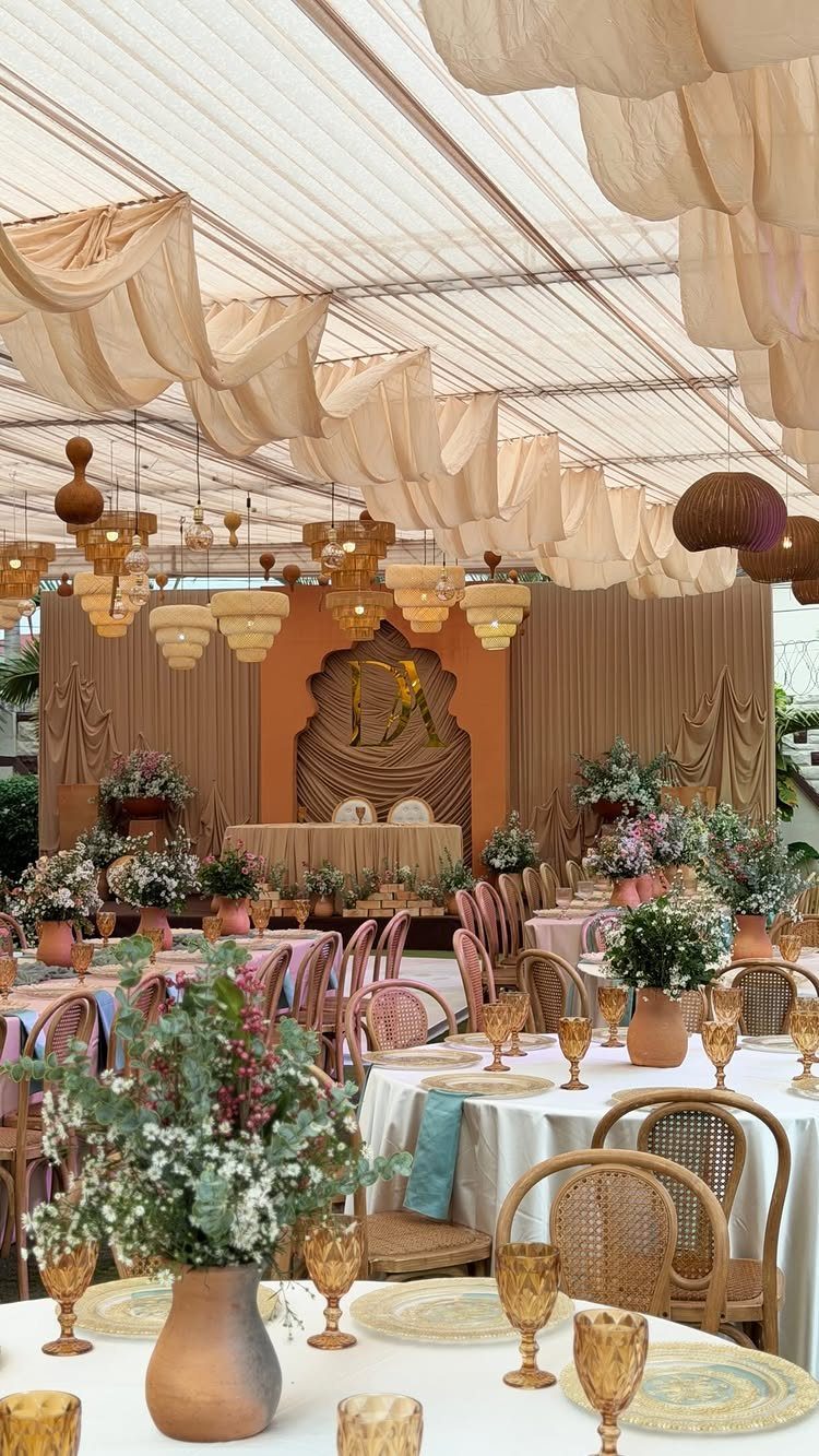 Wedding tent interior with rattan chairs, terracotta floral centerpieces, and wooden carved backdrop.