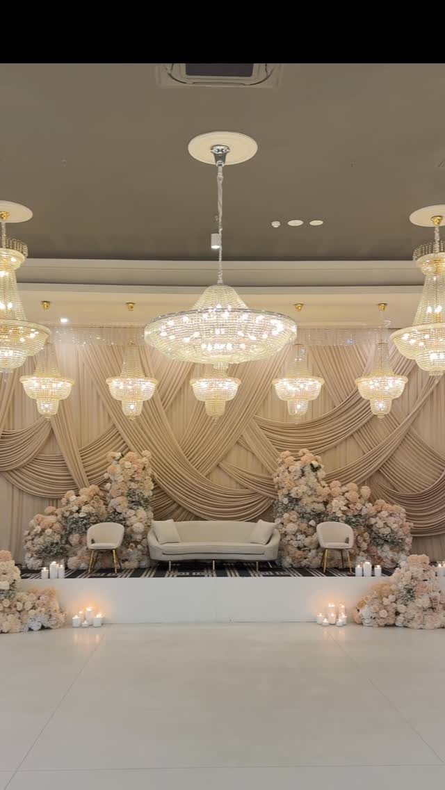 Wedding stage with champagne draped backdrop, blush roses, and crystal chandeliers.