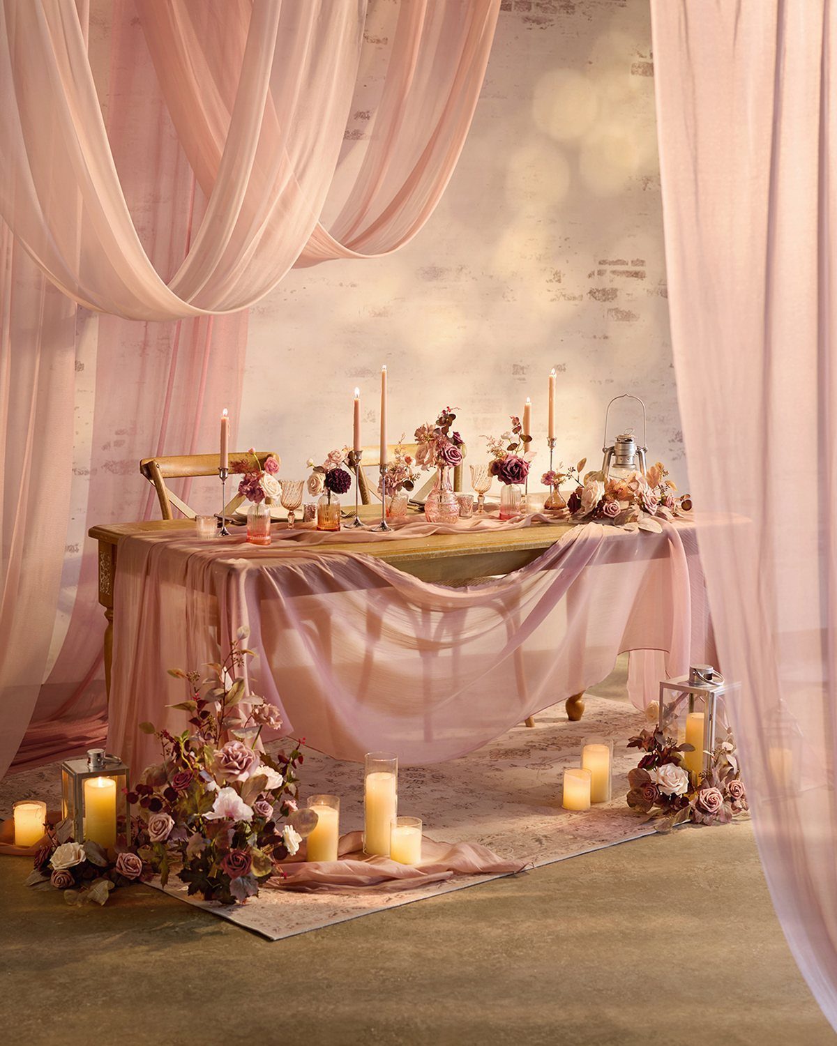 Romantic table setting with pink draped fabrics, rose floral arrangements, and glowing candles.