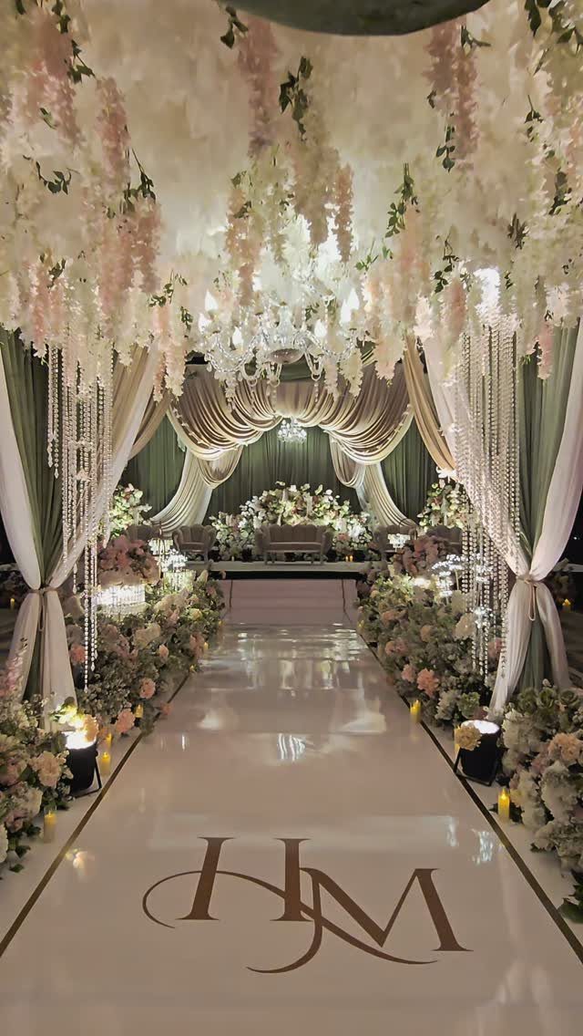 Wedding venue with sage green drapes, white floral ceiling, and glossy monogrammed aisle.