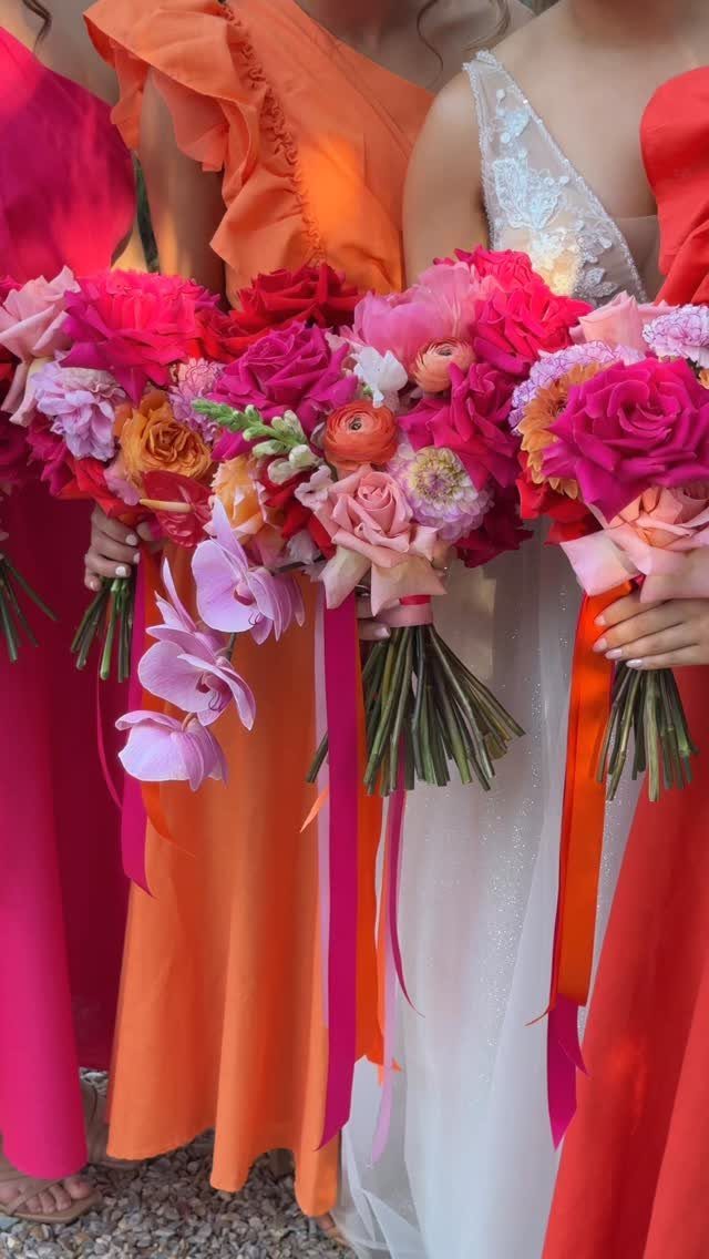Women in bright pink and orange dresses holding vibrant floral wedding bouquets.