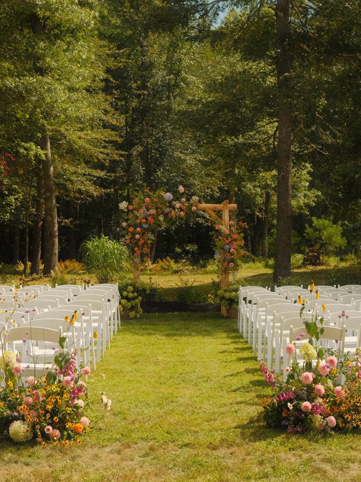 Outdoor wedding ceremony setup with white chairs and floral arch in a meadow