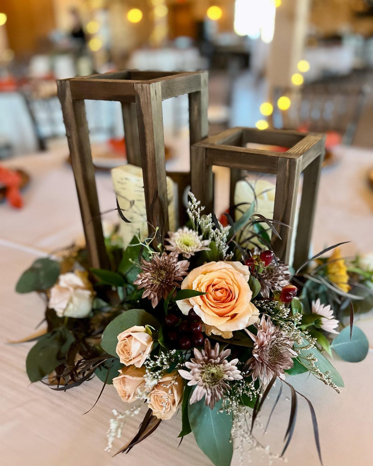Wooden lanterns and peach roses floral arrangement as a rustic wedding table centerpiece