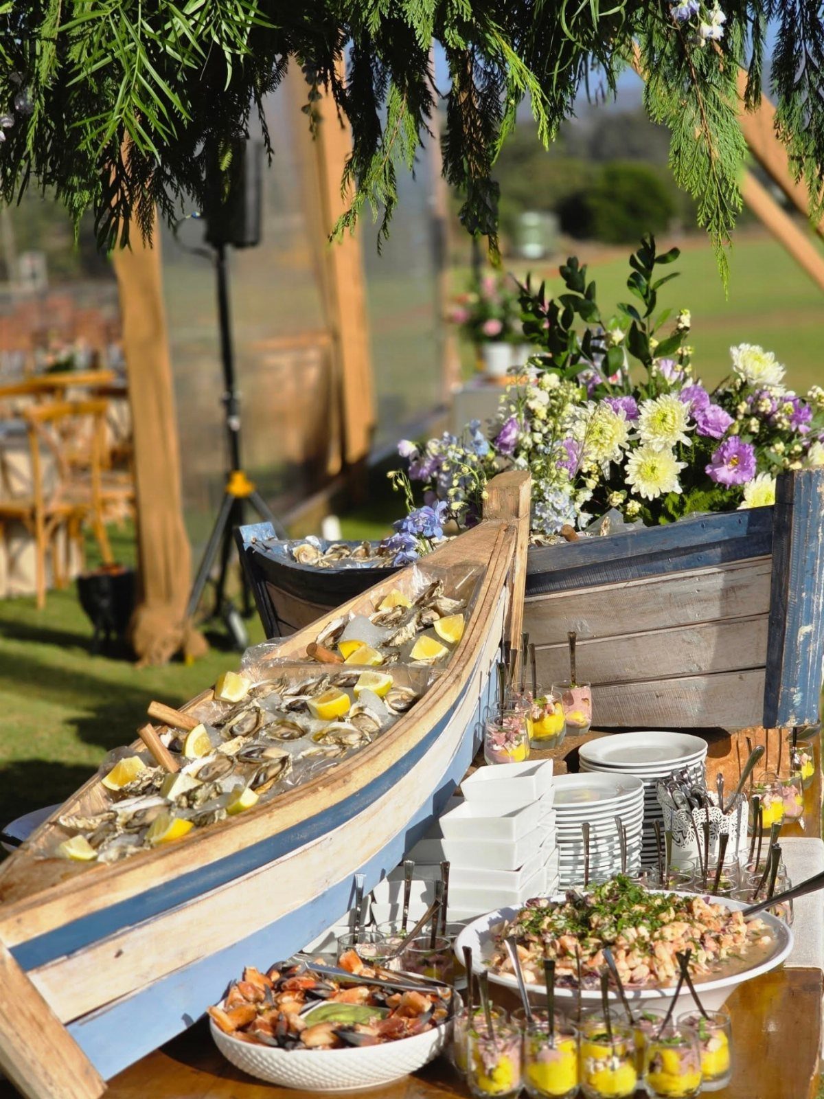 Seafood appetizers served in blue wooden boats on ice at an outdoor event.