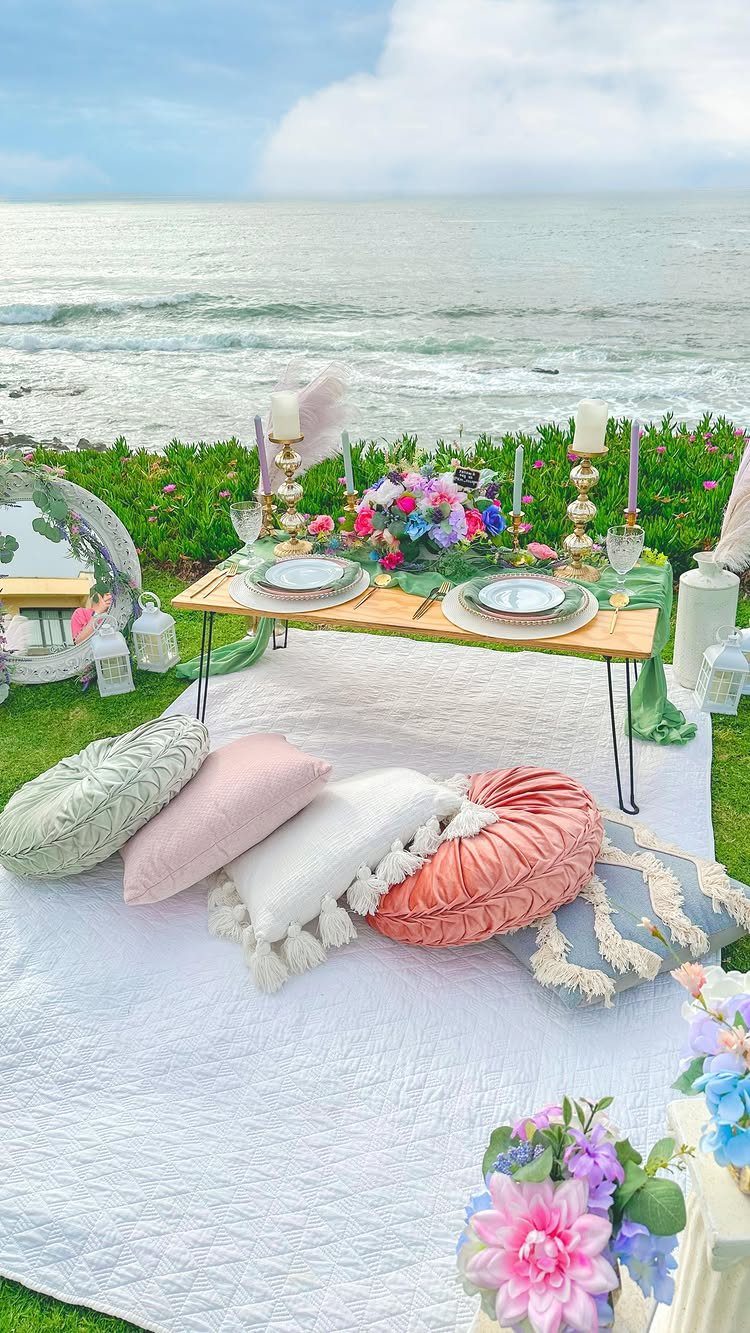 Romantic beach picnic setup with a low table, colorful pillows, and ocean view.